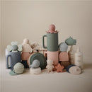 Silicone drain stoppers in blush and shifting sand colors, featuring playful designs and various shapes.