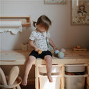 Child sitting on a wooden table, holding a cupcake toy, with a set of silicone cupcake toys and playful decor in the room.