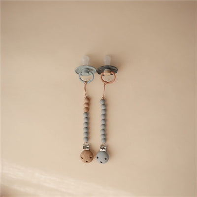 Mushie Eva Pacifier Clip in stone color, featuring two clips with wooden and silicone beads attached to pacifiers.