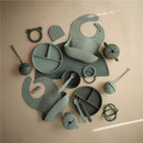 Mushie Silicone Pacifier Holder Case in Cambridge Blue, surrounded by various silicone feeding accessories.