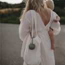 Mushie Silicone Pacifier Holder Case in Dried Thyme, attached to a beige tote, worn by a woman carrying a baby.
