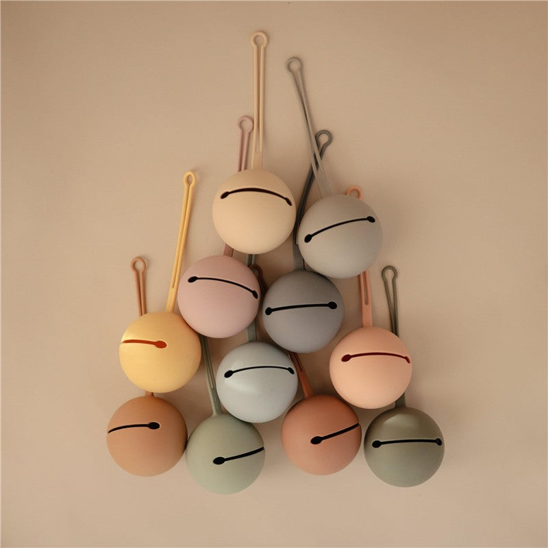 Mushie Silicone Pacifier Holder Cases in various pastel colors, arranged in a visually appealing manner on a neutral background.