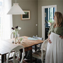A woman stands beside a rustic wooden dining table adorned with flowers and candles, featuring a blue silicone placemat.