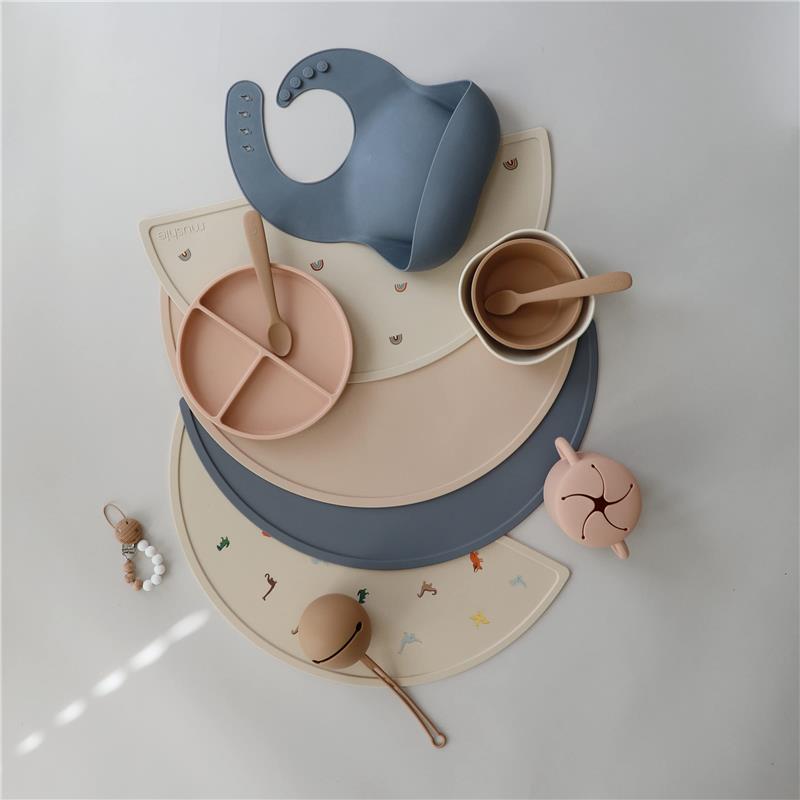 Mushie silicone placemat featuring a planets design, with a gray bib, divided peach plate, and various utensils.