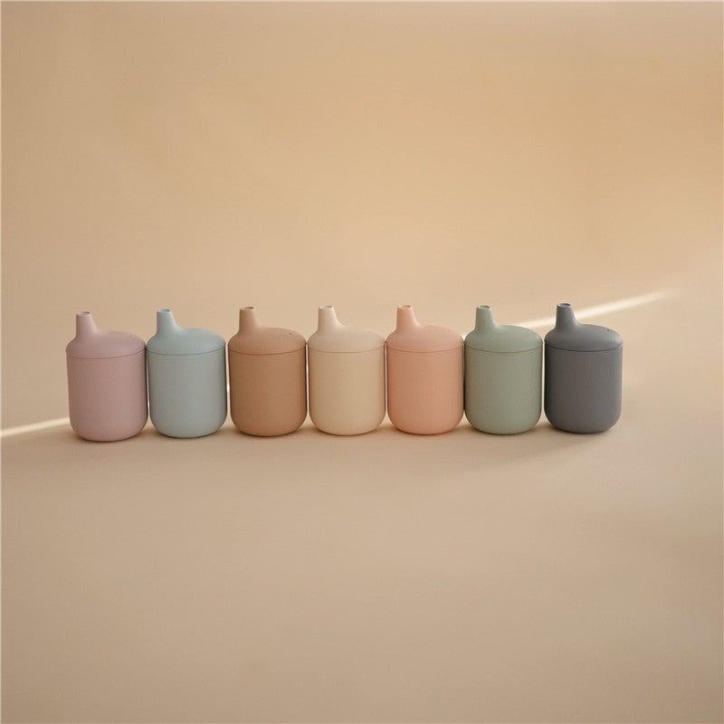 Silicone sippy cups in various pastel colors arranged in a line on a soft background.