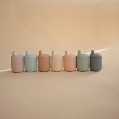 Silicone sippy cups in various pastel colors, including powder blue, arranged in a line against a soft background.
