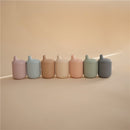 Silicone sippy cups in various pastel colors, including powder blue, arranged in a line against a soft background.