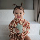 Smiling baby wearing a striped outfit, holding a powder blue Mushie silicone sippy cup.