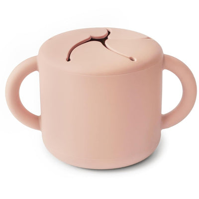 Mushie Silicone Snack Cup in blush color, featuring a lid with a split opening and easy-grip handles.