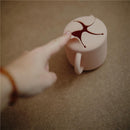 Silicone snack cup in blush color with a lid featuring a large opening, being touched by a finger.