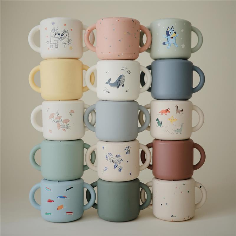 Colorful stack of Mushie silicone snack cups featuring playful designs including animals and patterns, suitable for kids.