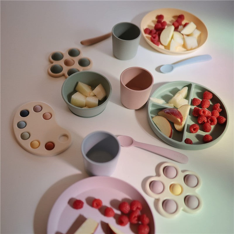 Silicone suction bowls and cups in pastel colors, displaying fruit and snacks on a white surface.