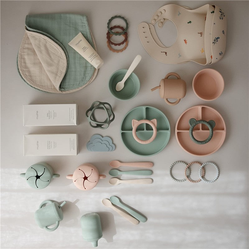 Silicone suction bowl in Cambridge Blue among various baby feeding products, including utensils, bibs, and teething rings.