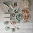 Silicone suction bowl in Cambridge Blue among various baby feeding products, including utensils, bibs, and teething rings.