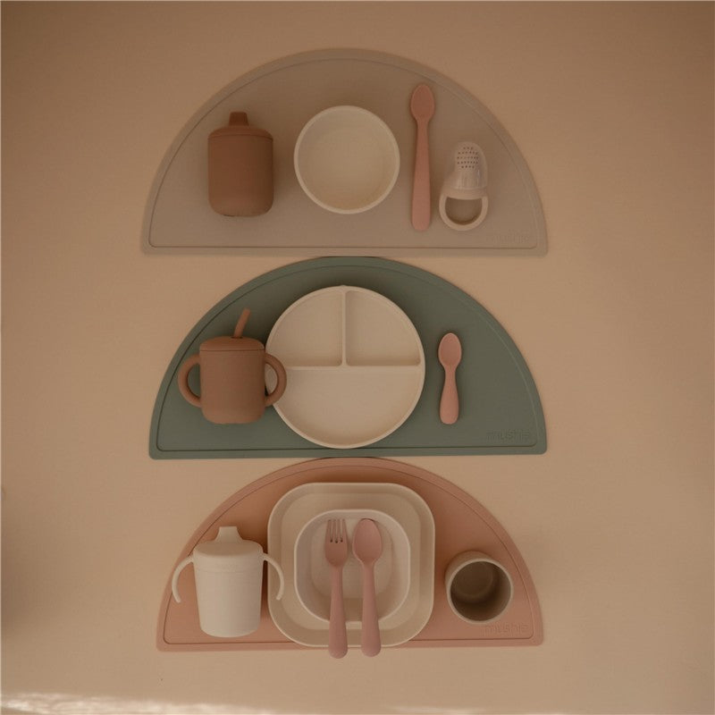 Mushie Silicone Suction Plates in ivory, featuring three plates with various utensils and cups arranged neatly.