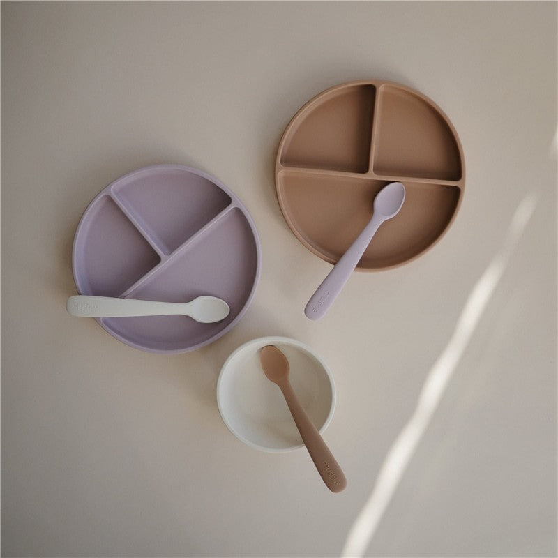 Silicone suction plates in soft lilac, brown, and white with matching spoons, displayed on a neutral background.