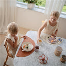 Two young girls seated at a marble table, one with a Mushie silicone suction plate in soft lilac, enjoying sushi.