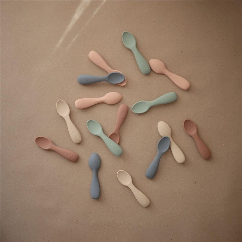 Silicone toddler starter spoons in natural and shifting sand colors, featuring a soft, child-friendly design.
