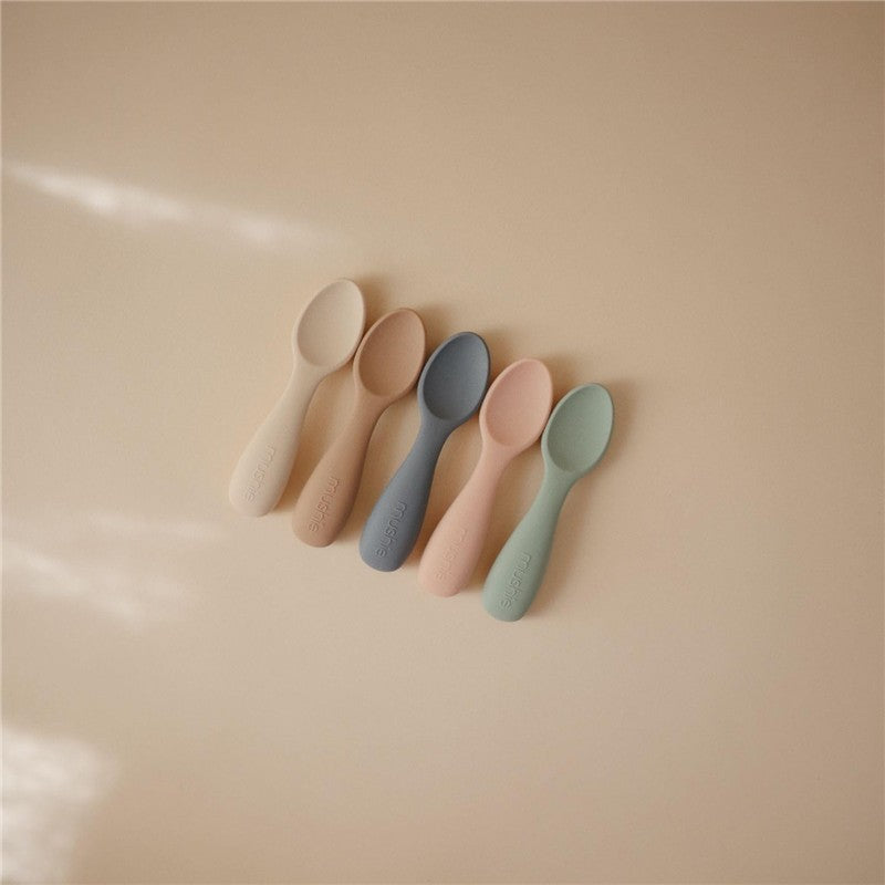 Silicone toddler starter spoons in natural and shifting sand colors, arranged on a neutral background.