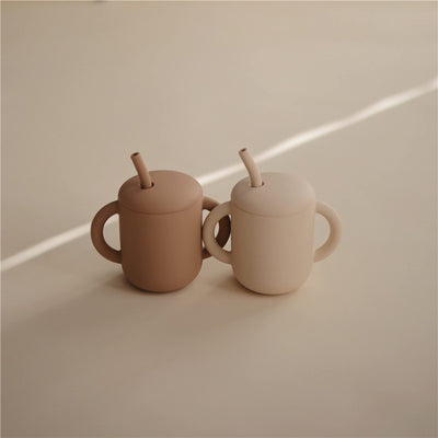 Silicone training cups in natural colors, featuring a straw and easy-to-grip handles for children.