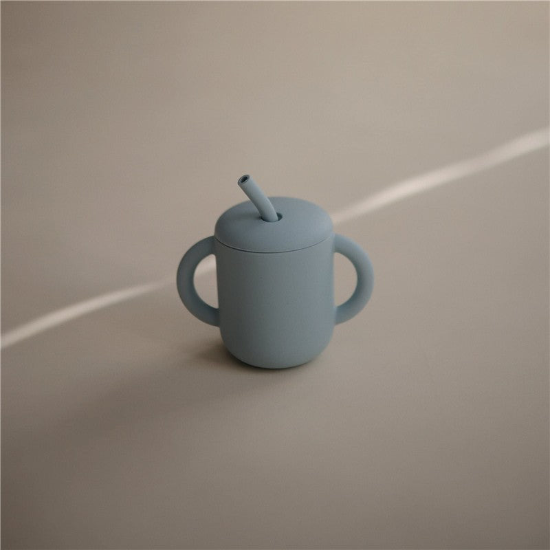 Mushie Silicone Training Cup in powder blue with two handles and a straw, designed for young children.