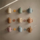 Silicone training cups in various colors, including powder blue, displayed on a wall with matching lids and straws.