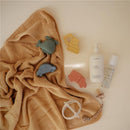 Mushie Vehicles Mold-Free Bath Play Set 4-Pack with colorful bath toys on a beige towel, featuring a bottle of baby body lotion.