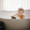 Child playing with a gray car and yellow vehicle toy in a bath, enjoying the Mushie Mold-Free Bath Play Set.