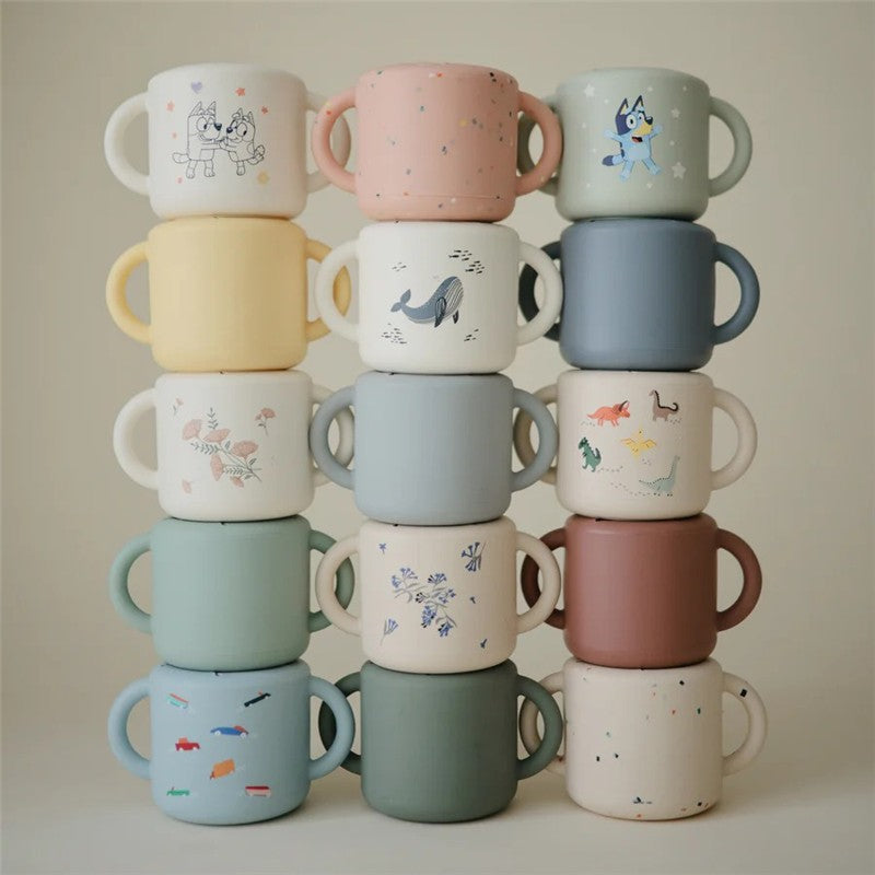 Mushie Snack Cup set featuring various colors and playful designs, including animals and abstract patterns, stacked neatly.