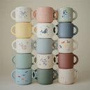 Mushie Snack Cup set featuring various colors and playful designs, including animals and abstract patterns, stacked neatly.