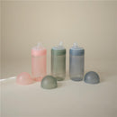 Mushie Soft Spout Sippy Cups in pink, green, and blue, with matching lids, arranged on a neutral background.