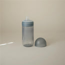 Mushie Soft Spout Sippy Cup in Tradewinds color, featuring a transparent body and a soft spout lid, with a dome cap nearby.