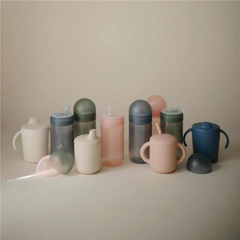 Mushie Soft Spout Sippy Cups in various pastel colors, featuring soft spouts and ergonomic handles for easy grip.