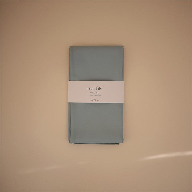 Mushie Splat Mat in Roman Green, neatly folded with a white label displaying the brand name and product details.