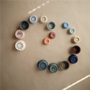 Mushie Stacking Cups in various colors arranged in a spiral pattern, showcasing their playful designs and textures.
