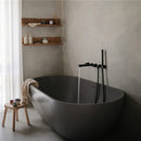 A modern bathroom featuring a sleek gray bathtub with water running from black faucets, a wooden stool holding colored cups, and minimalist decor.