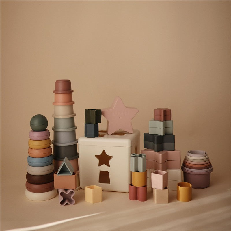 Mushie Stacking Rings in rustic colors, featuring various shapes and sizes for sensory play and stacking fun.
