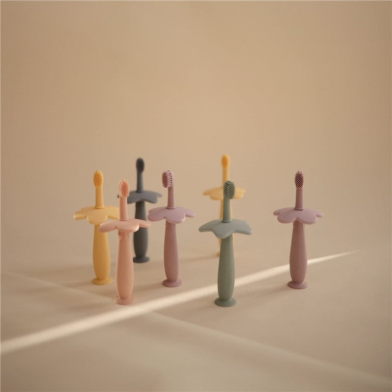 Soft lilac silicone flower training toothbrush among pastel-colored toothbrushes, designed for toddlers.