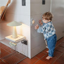 Child in a blue and white checkered sweater interacts with a Mushie Sunshine Suction Spinner Toy on a wall.