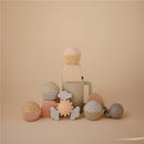 Colorful silicone toys including a sun, clouds, and cupcakes arranged around a beige cup, designed for sensory play.