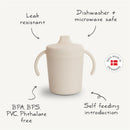 Mushie Trainer Sippy Cup in Cloud color, featuring handles and notes on being leak resistant, dishwasher safe, and BPA-free.