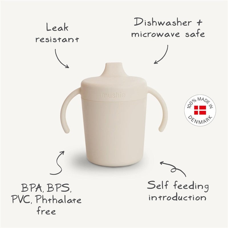Mushie Trainer Sippy Cup in ivory, featuring ergonomic handles, leak resistance, and labels highlighting safety and usability.