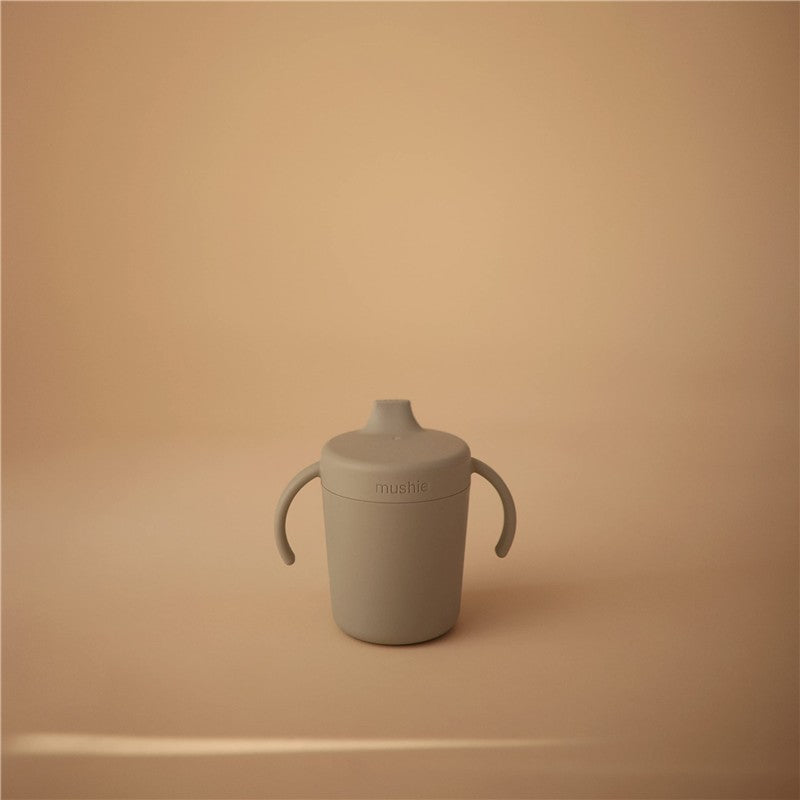 Mushie Trainer Sippy Cup in sage color, featuring two handles and a removable top, displayed against a neutral background.
