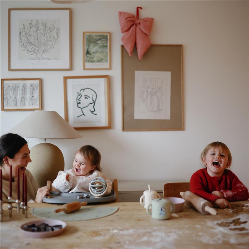 A mother and two happy children sit at a dining table covered in flour, enjoying a playful baking activity together.