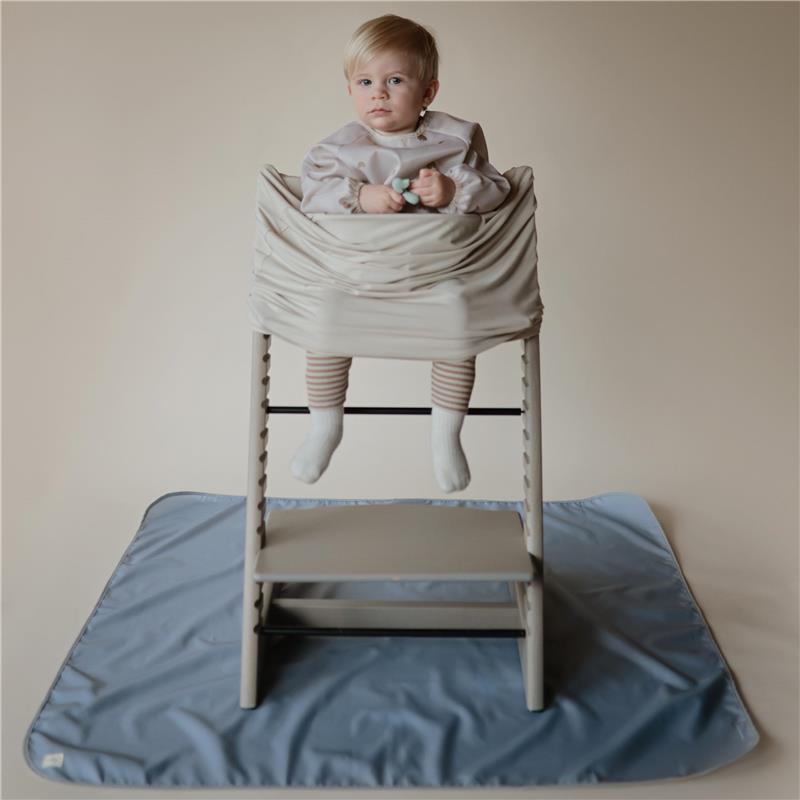 Baby sitting in a high chair wearing a long sleeve water-resistant bib with a cherry print, on a blue mat.