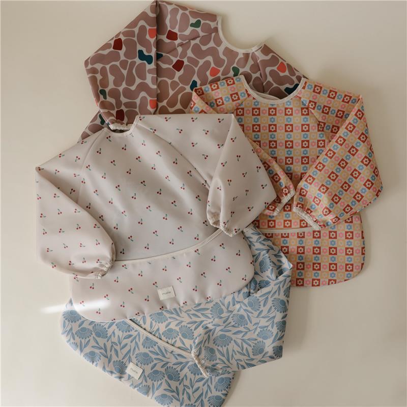 Water-resistant adjustable baby bibs in various patterns, including one with cherries, stacked on a light background.