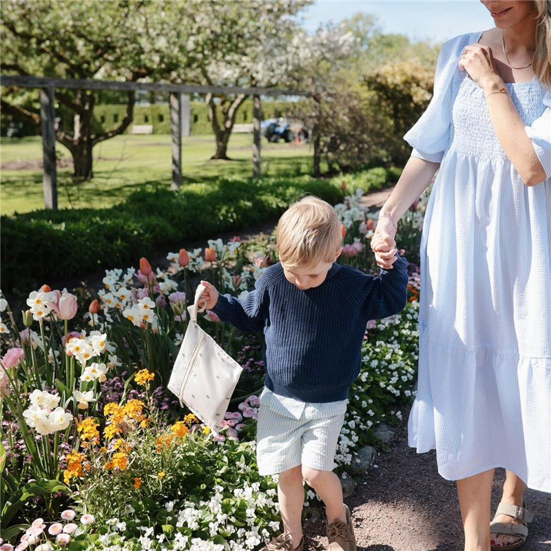 Mother and child walking in a flower garden, child holding a Mushie water-resistant wet bag in a floral design.