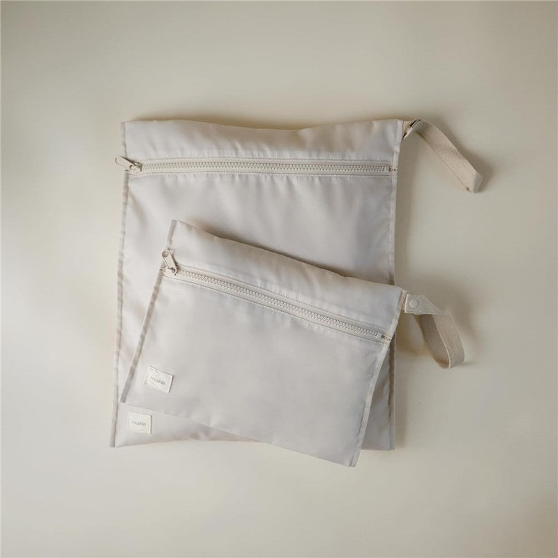 Mushie water-resistant wet bags in fog color, featuring two sizes with zippers and handles for easy carrying.