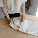 Mushie water-resistant wet bag in Roman Green, being filled with fabric items on a wooden table.