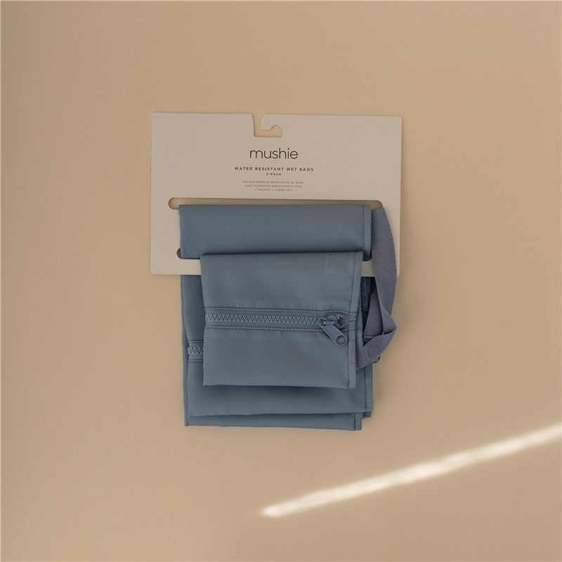Mushie water-resistant wet bags in two shades of blue, featuring a zippered pocket and a hanging strap.